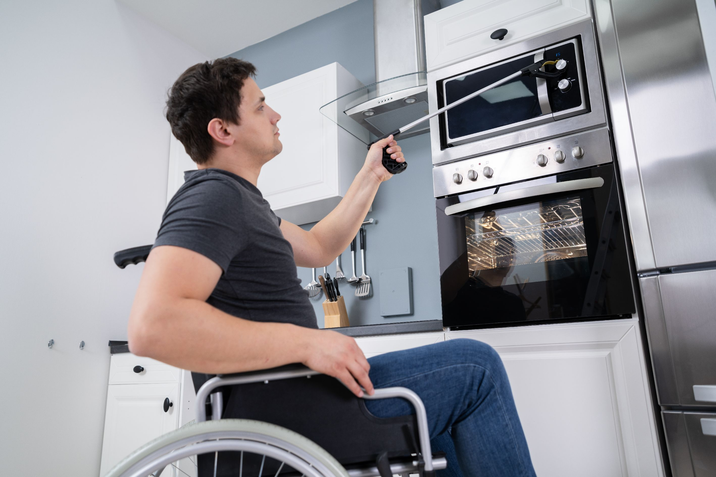 Man in wheelchair in kitchen using a device to reach up